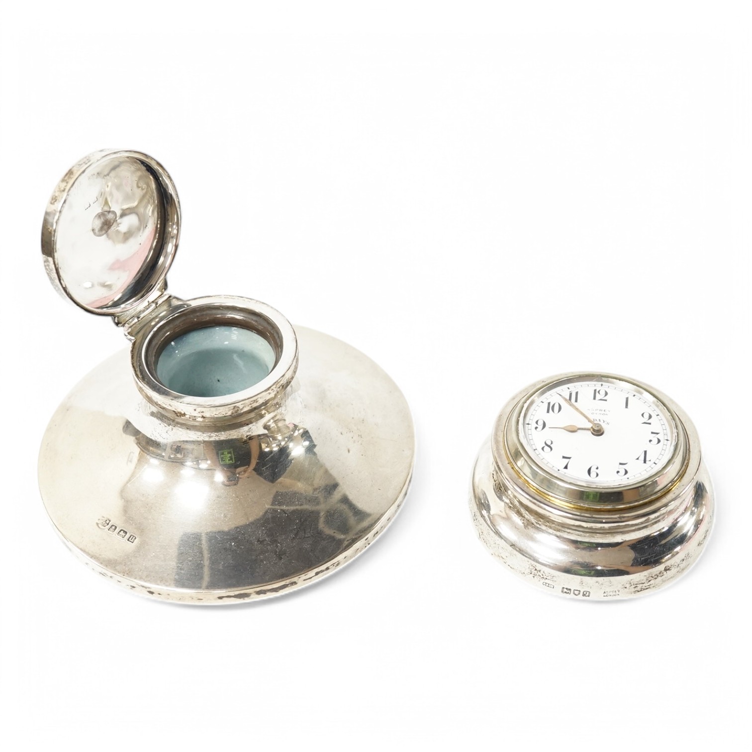 A George V Asprey & Co silver mounted brass cased timepiece, with Arabic dial and 8-day movement, the mount hallmarked for London, 1911, base diameter 72mm, together with a George V silver mounted capstan inkwell. Condit